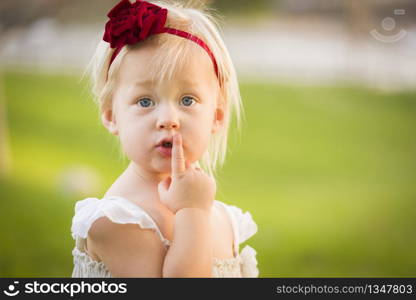 Beautiful Adorable Little Girl With Her Finger on Her Mouth Wearing White Dress In A Grass Field.