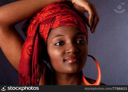 Beautiful African-American woman wearing a traditional tribal red orange head scarf and big orange hoop earrings, with arm over her head, isolated.