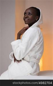 Beautiful african spa woman wearing bathrobe sitting on the couch at beauty salon