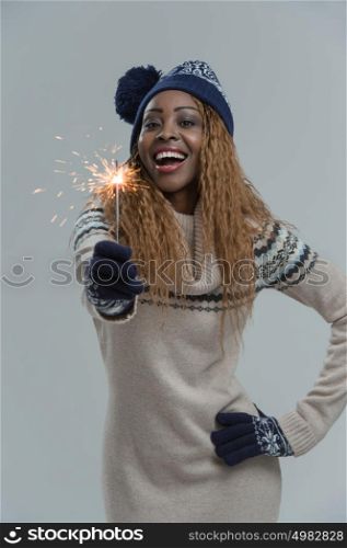 Beautiful african winter woman holding sparkler on gray background
