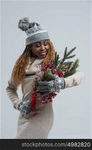 Beautiful african woman in studio wearing winter knitted dress and hat and holding winter bouquet