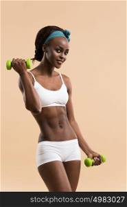 Beautiful african woman pumping up muscles with dumbbells