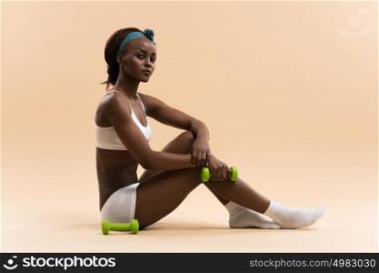 Beautiful african woman pumping up muscles with dumbbells