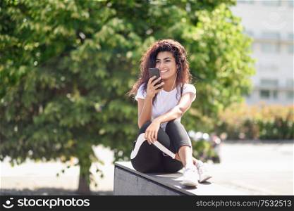 Beautiful African woman recording a voice note with smart phone outdoors. Arab girl in sport clothes with curly hairstyle in urban background.. African woman recording a voice note with smart phone