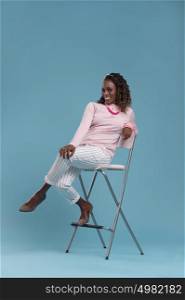 Beautiful african woman wearing pink clothes and high heels, sitting on a chair. Studio shot.