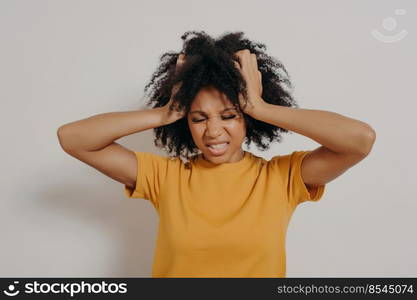 Beautiful african young woman standing in casual clothes angry and mad, screaming frustrated and furious while holding her head with hands, shouting with anger. Rage and aggressive concept. Beautiful african young woman standing in casual clothes angry and mad, screaming in anger