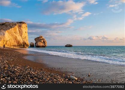 Beautiful afternoon view of the beach around Petra tou Romiou, in Paphos, Cyprus with a boy strolling in the distance. It is considered to be Aphrodite&rsquo;s birthplace in Greek mythology.
