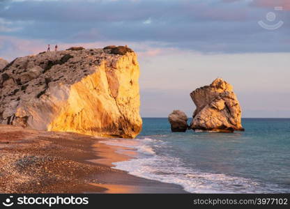 Beautiful afternoon view of the beach around Petra tou Romiou, in Paphos, Cyprus with people climbing the rock in the distance. It is considered to be Aphrodite&rsquo;s birthplace in Greek mythology.