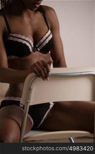 Beautiful alluring african woman in sexy lingerie. Portrait of beautiful sexy stylish young woman model with perfect clean skin in black lingerie posing on chair