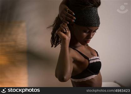 Beautiful alluring african woman in sexy lingerie. Portrait of beautiful sexy stylish young woman model with perfect clean skin in black lingerie posing at home through palm tree