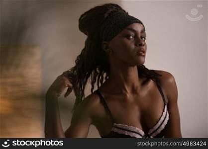 Beautiful alluring african woman in sexy lingerie. Portrait of beautiful sexy stylish young woman model with perfect clean skin in black lingerie posing at home through palm tree