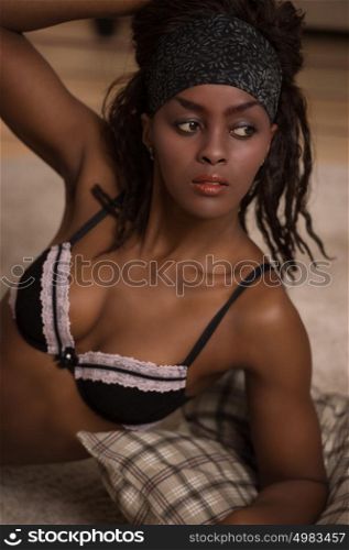 Beautiful alluring african woman in sexy lingerie. Portrait of beautiful sexy stylish young woman model with perfect clean skin in black lingerie posing on floor at home with pillow