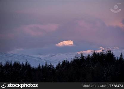 Beautiful Alpen Glow hitting mountain peaks in Scottish Highlands during stunning Winter landscape sunrise