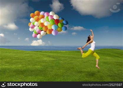 Beautiful and athletic girl jumping with balloons on a green meadow