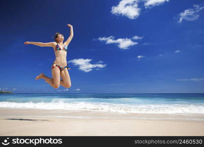 Beautiful and athletic young woman enjoying the summer, jumping in a tropical beach