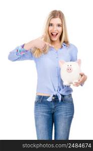 Beautiful and attractive blonde woman holding and pointing to a piggy bank, isolated over white background