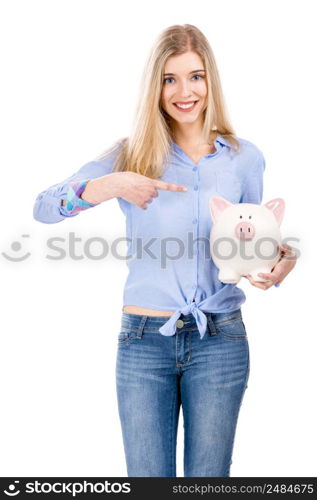 Beautiful and attractive blonde woman holding and pointing to a piggy bank, isolated over white background