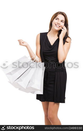 Beautiful and attractive young woman with arms up holding shopping bags and making a call, isolated over white background