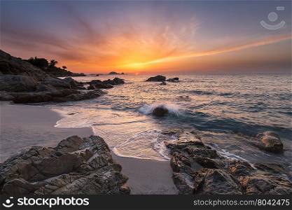 Beautiful and dramatic sunset over Ile Rousse in the Balagne region of Corsica with beach, rocks and the Mediterranean sea in the foreground