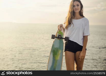 Beautiful and fashion young woman posing at the sunset with a skateboard