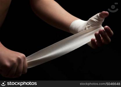 Beautiful and fit female fighter getting prepared for the fight or training, wrapping her hands with bandage tape against dark background.