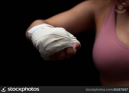 Beautiful and fit female fighter getting prepared for the fight or training, holding wrapped fist ready for punch against dark background.