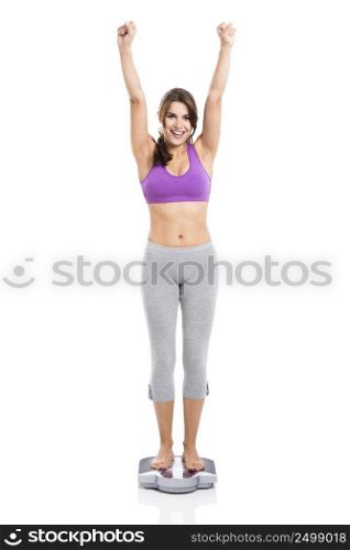 Beautiful and happy athletic woman over a scale with arms up, isolated on white background