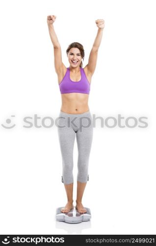 Beautiful and happy athletic woman over a scale with arms up, isolated on white background