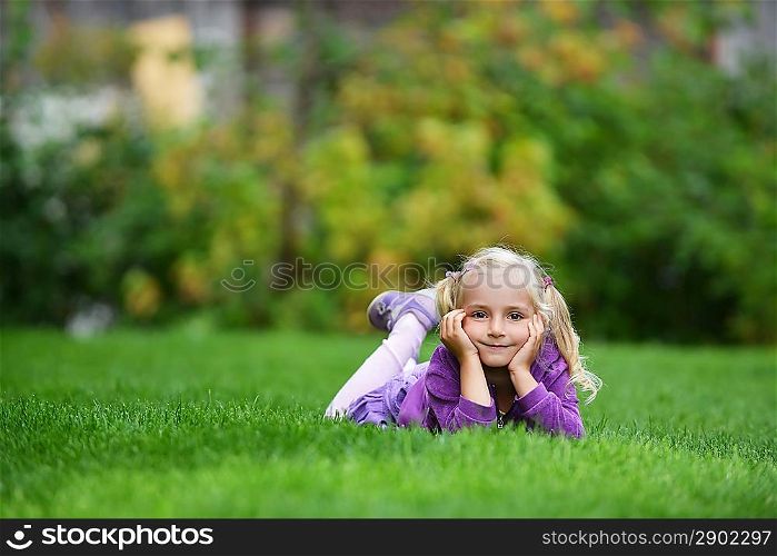 beautiful and happy little girl lying on green grass