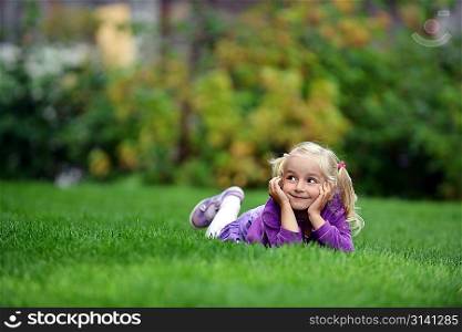 beautiful and happy little girl lying on green grass