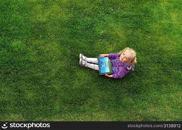 beautiful and happy little girl sitting on grass with laptop computer