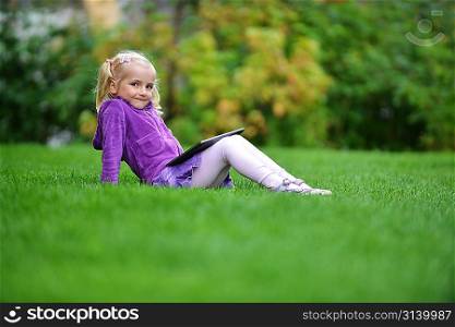beautiful and happy little girl sitting on grass with laptop computer
