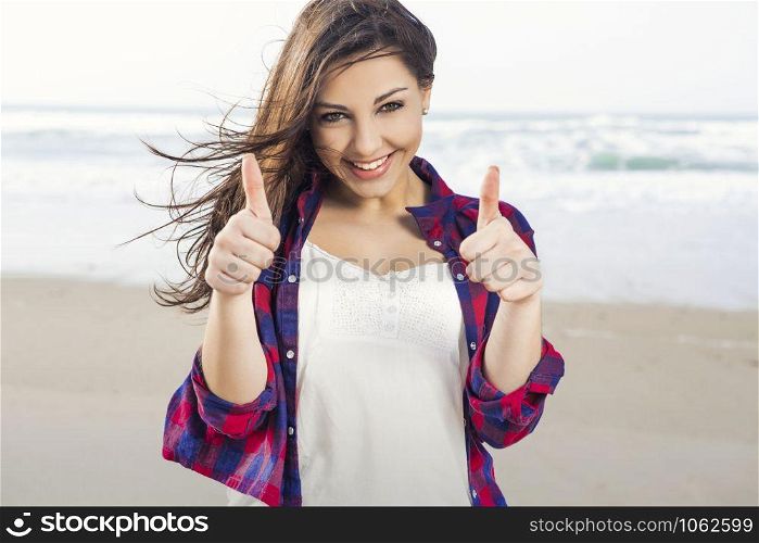 Beautiful and happy teen at the beach with thumbs up