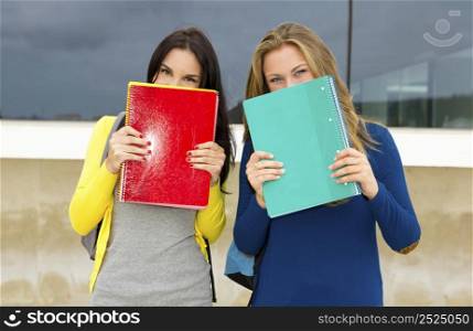 Beautiful and happy teenagers students covering the faces with school books