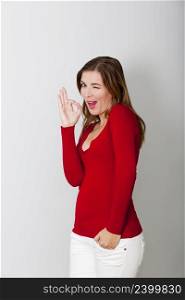 Beautiful and happy woman doing a okay signal, against a gray wall