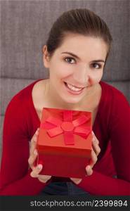 Beautiful and happy woman on the sofa holding a christmas present