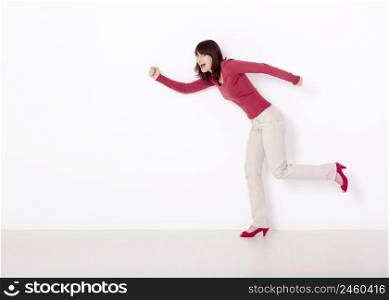 Beautiful and happy woman simulating she&rsquo;s running against a white wall