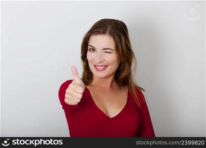 Beautiful and happy woman with thumbs up, against a gray wall