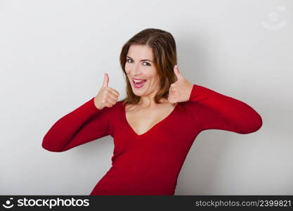 Beautiful and happy woman with thumbs up, against a gray wall