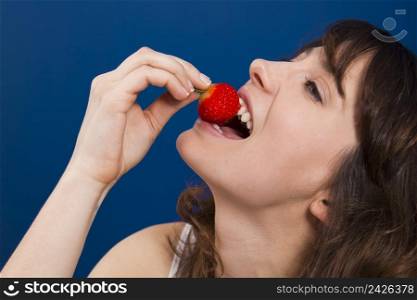 Beautiful and happy young woman eating a strawberry with taste