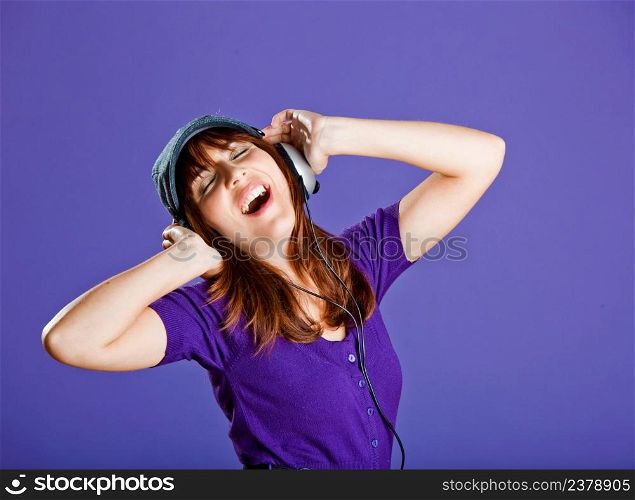 Beautiful and happy young woman listen music with headphones, over a violet background