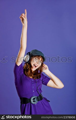 Beautiful and happy young woman listen music with headphones, over a violet background