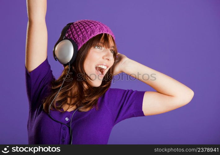 Beautiful and happy young woman listen music with headphones, over a violet background