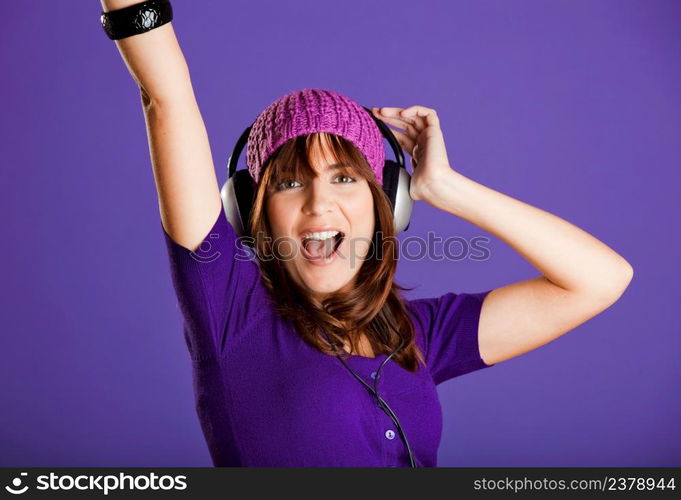 Beautiful and happy young woman listen music with headphones, over a violet background