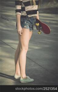 Beautiful and sexy street girl posing with her skateboard under her arms