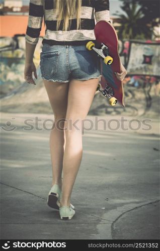 Beautiful and sexy street girl walking with her skateboard under her arms