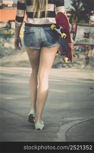 Beautiful and sexy street girl walking with her skateboard under her arms