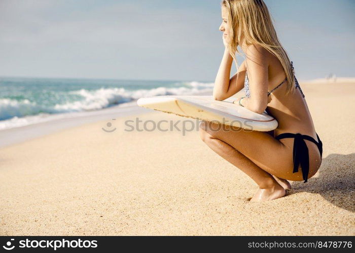 Beautiful and sexy surfer girl holding a surfboard and checking the waves