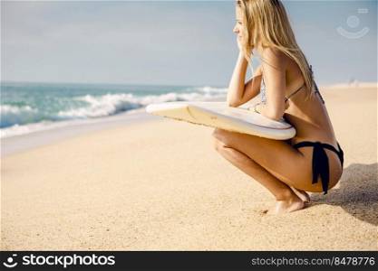 Beautiful and sexy surfer girl holding a surfboard and checking the waves