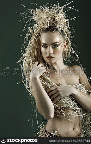 beautiful and sexy woman with raffia hair and a ethnic costume in a shot over dark with creative gold make up